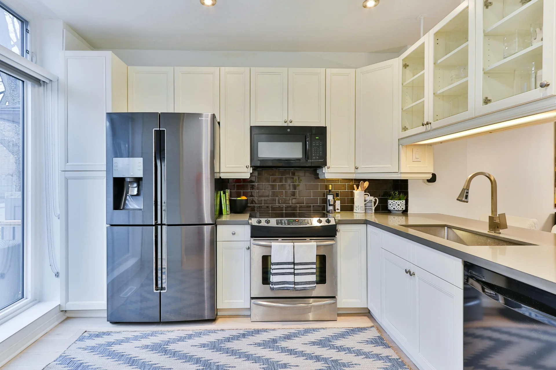Modern bright kitchen interior with a large side-by-side stainless steel refrigerator, built-in stove, and white cabinetry.